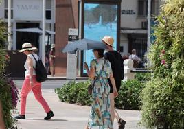 Turistas se protegen del sol en Málaga con un paraguas, este domingo.