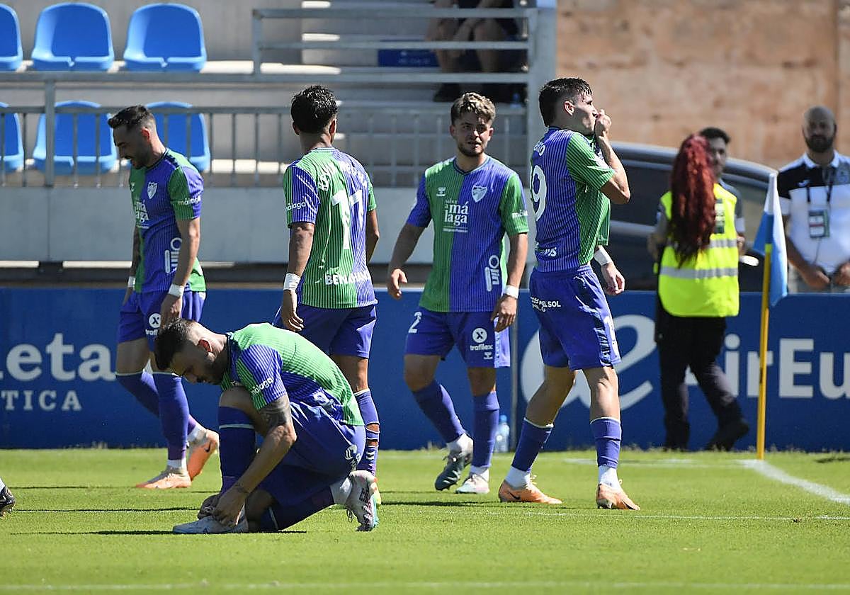 Roberto besa el escudo del Málaga tras marcar su gol ante el Atlético Baleares mientras Dioni se anuda las botas.