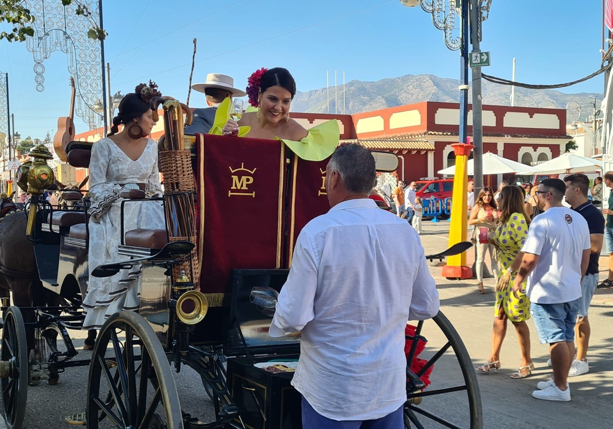 Una mujer, vestida de flamenca y con una copa de fino en la mano, charla desde el coche de caballos en el recinto ferial de Fuengirola.