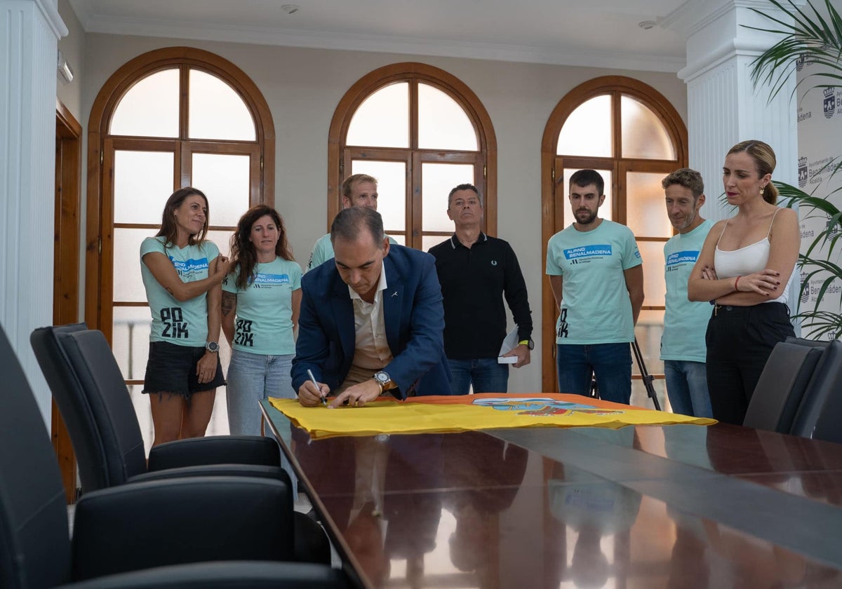 El alcalde de Benalmádena firma una bandera de la localidad antes de regalársela a deportistas del municipio.