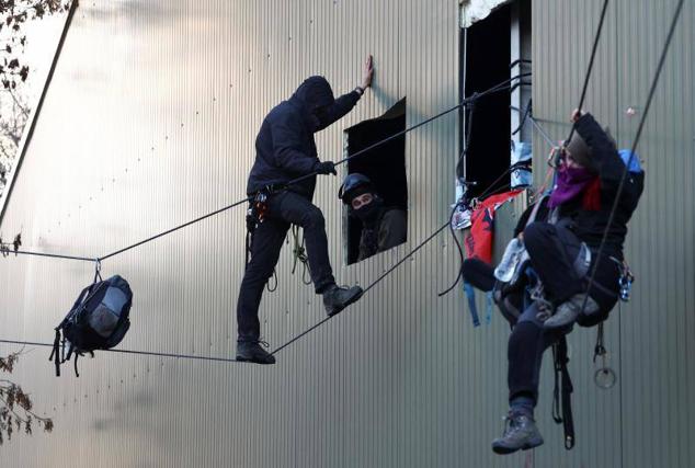 Un activista sujetado con un arnés a una cuerda se apoya en la pared de un granero.