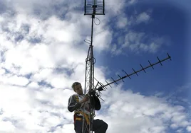 Un técnico trabaja sobre una antena de televisión instalada en un edificio.
