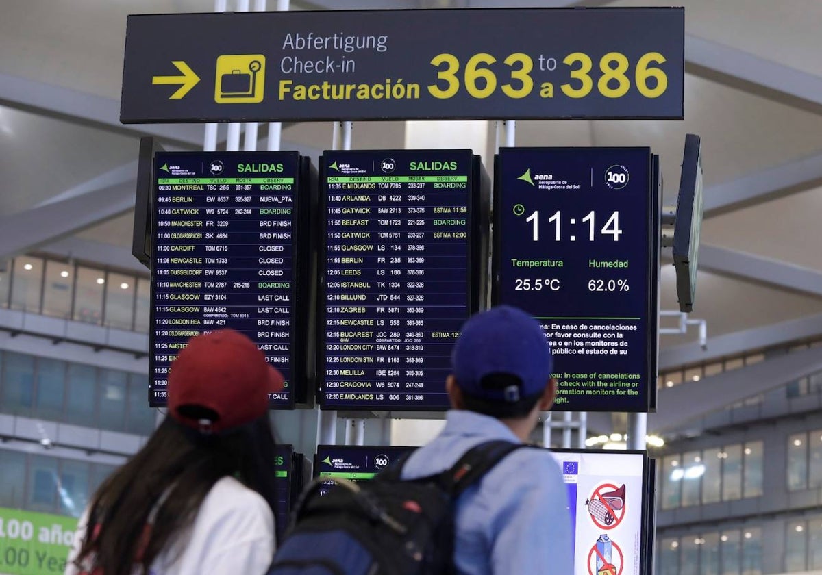 Unos jóvenes revisan sus vuelos en uno de los paneles informativos del aeropuerto.