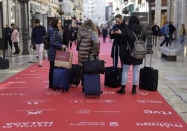 Visitantes con maletas en la alfombra roja del festival, en la calle Larios.