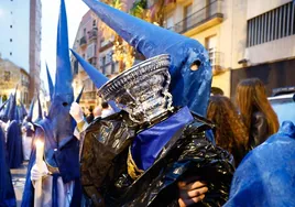 Un nazareno mojado por la lluvia protege un enser con una bolsa de plástico.