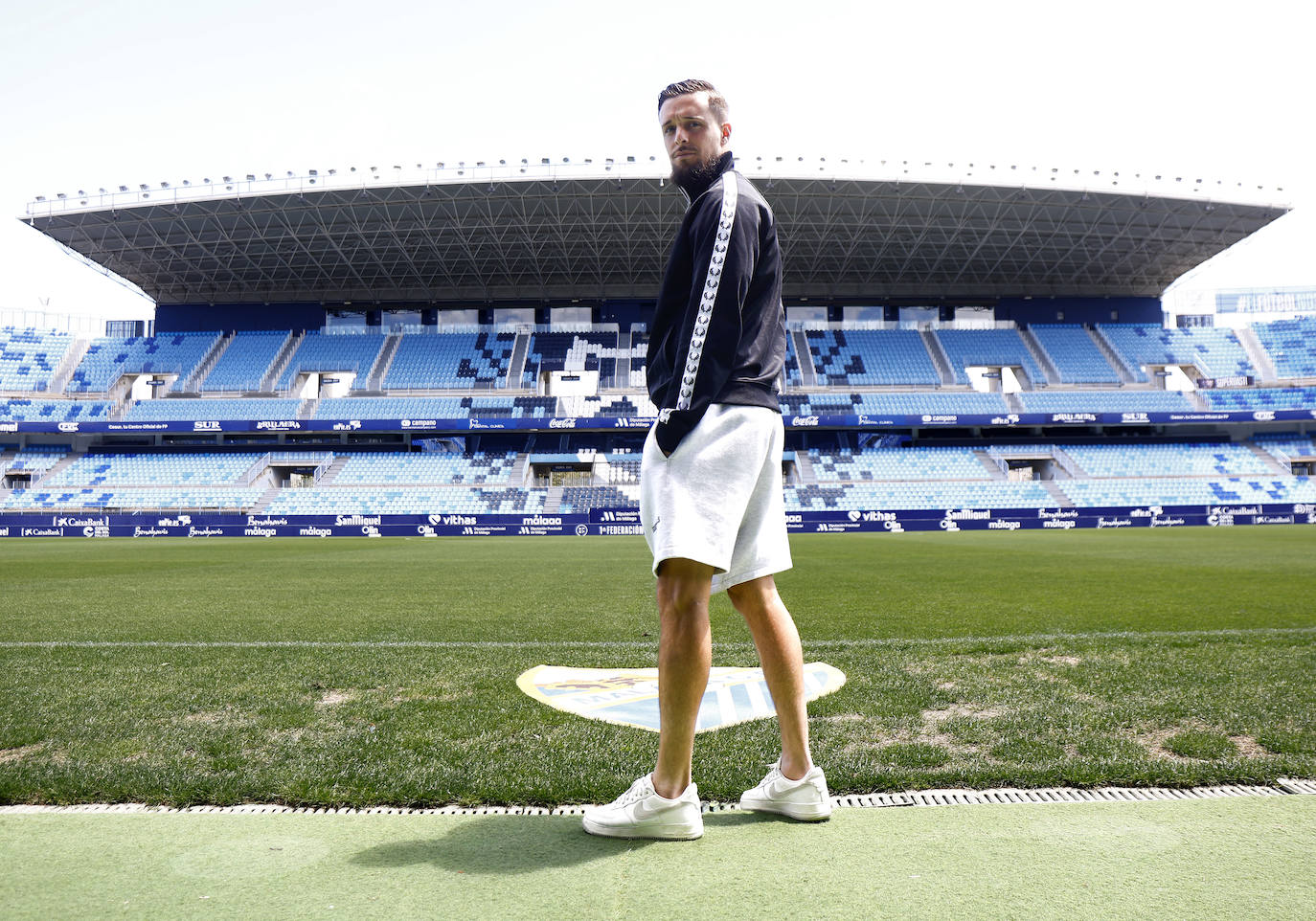 Genaro posa a ras de césped en La Rosaleda con la grada de Preferencia de fondo.