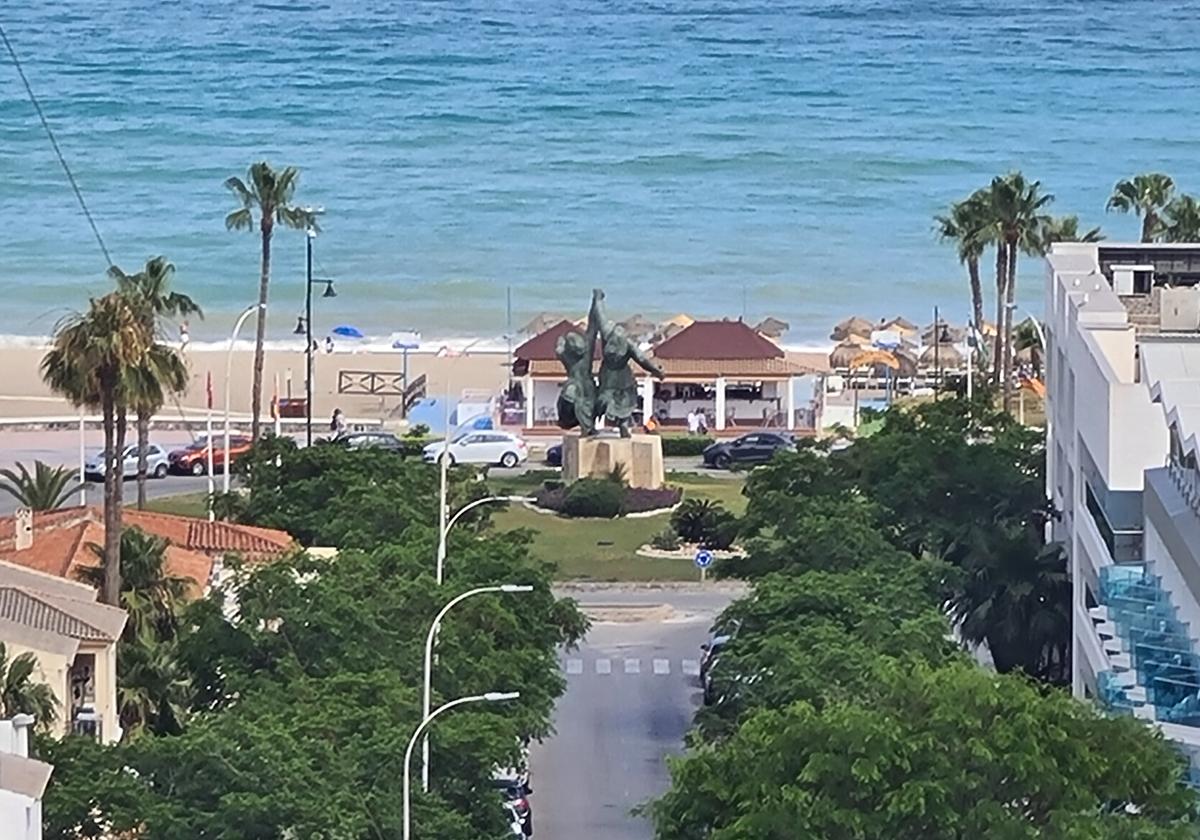 Vista de la playa de El Bajondillo, desde la calle Sierra de Estepa, con la escultura de las mujeres corriendo en el centro de la imagen.