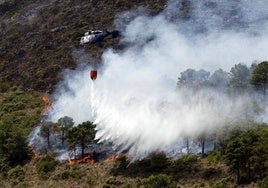 Un helicóptero de Infoca descarga sobre las llamas de un incendio forestal.