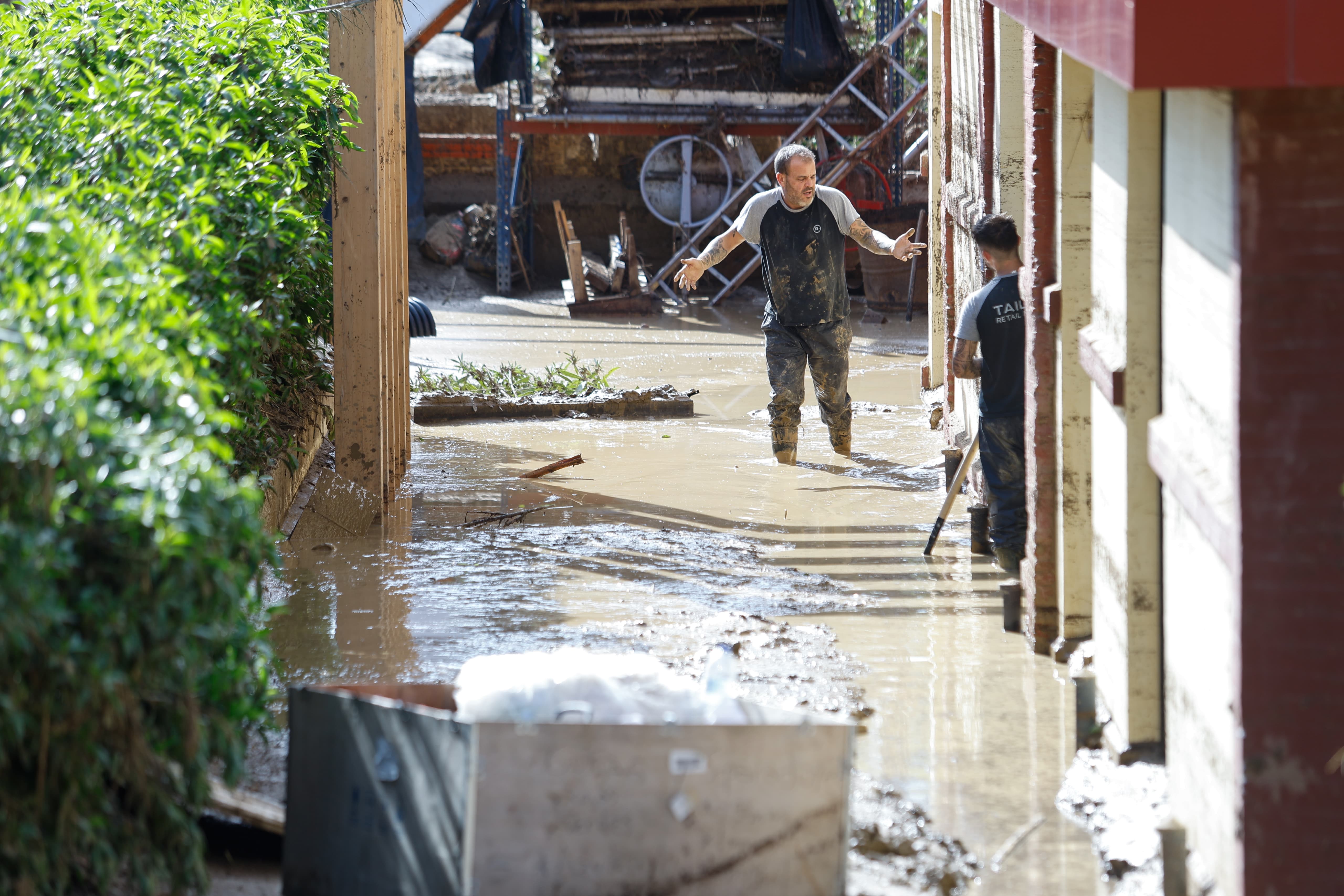 Dos personas limpian una zona inundada en Álora.