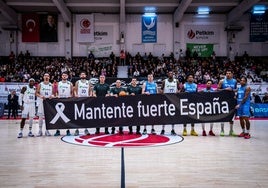 Jugadores de ambos conjuntos posan con una pancarta de apoyo.