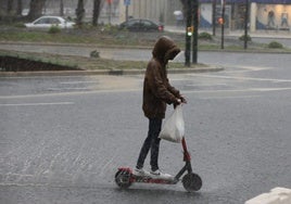 Un joven circula con un patinete eléctrico bajo la lluvia.