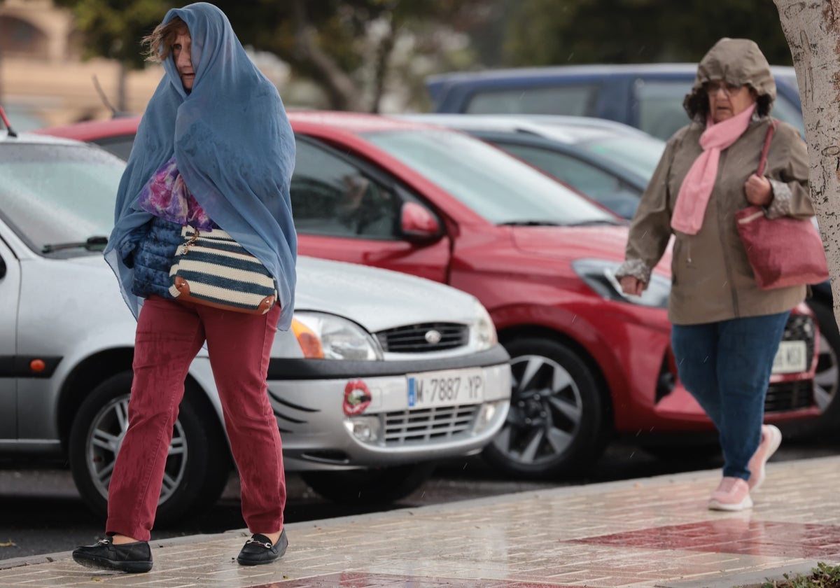 Dos mujeres caminan por la calle en Málaga mientras intentan protegerse de la lluvia.