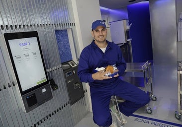 Ricardo Álvarez, junto a la pantalla de pedidos, con una de sus hamburguesas.