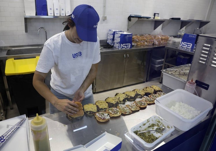 Una de las cocineras prepara algunas hamburguesas, de las que ofrecen tres variedades.