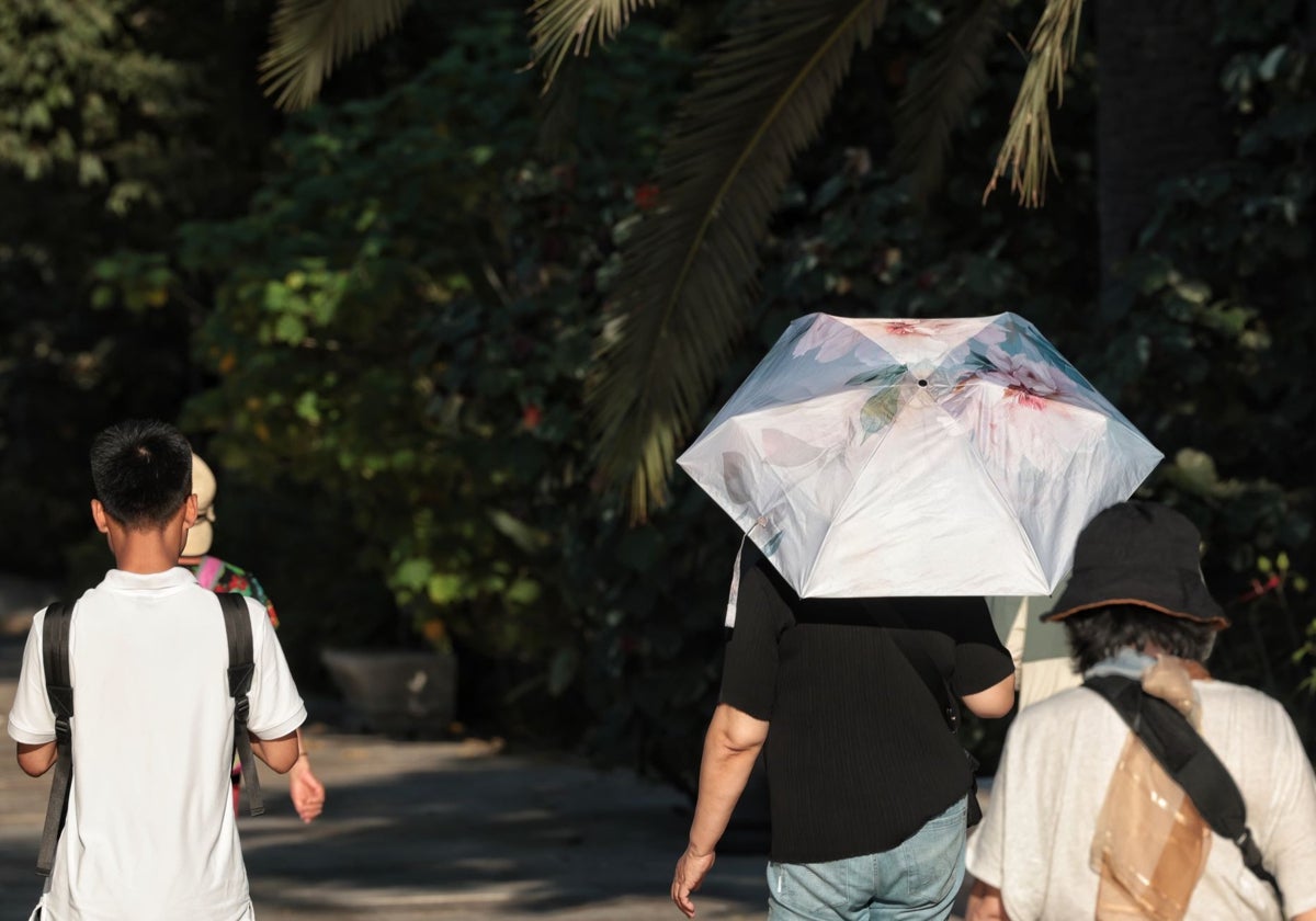 Un turista pasea bajo una sombrilla para protegerse del sol en el Parque de Málaga.