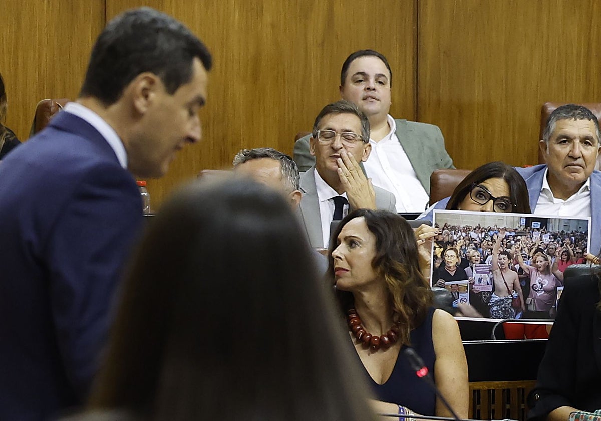 La socialista Ángeles Férriz enseña una foto de una manifestación mientras interviene Juanma Moreno