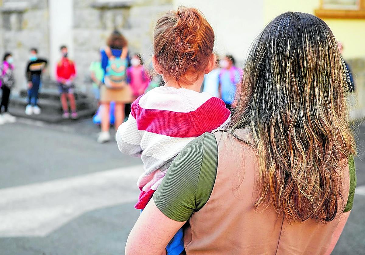 Una madre, con su hijo en brazos, en el patio de un colegio.