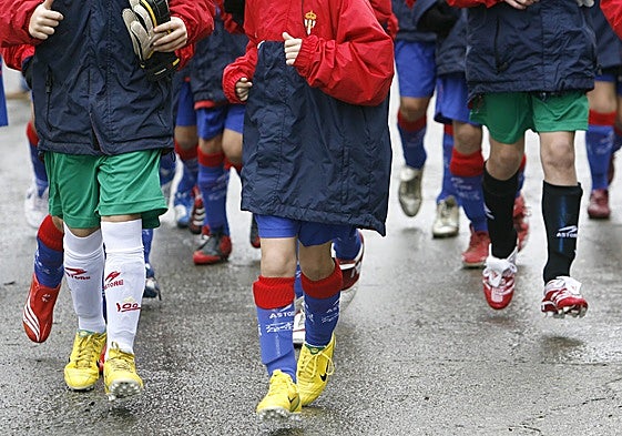 Unos niños pasean con botas de fútbol.