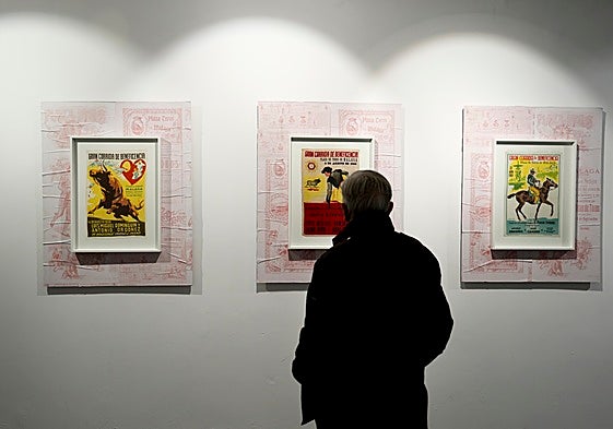 Un asistente a la muestra contempla tres de los carteles expuestos.