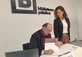Carlos San Millán, cronista de Alhaurín de la Torre firma un ejemplar de su libro, en presencia de directora de la Biblioteca Municipal 'Antonio Garrido Moraga', Rocío Serrán.