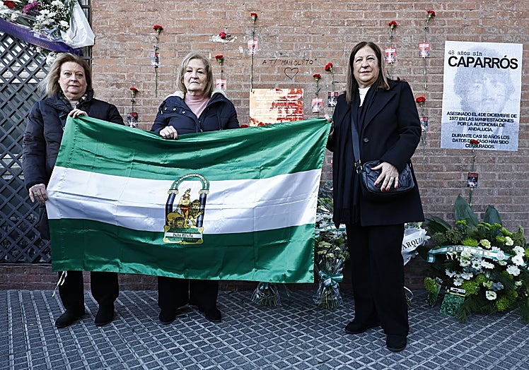 Puri, Paqui y Loli, con una bandera andaluza, esta mañana ante la placa que recuerda a su hermano en el lugar donde murió.