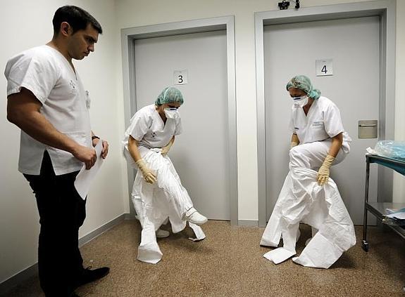 Dos auxiliares se colocan los trajes de protección en presencia de un instructor, durante los cursos de simulación en el Hospital La Fe de Valencia.