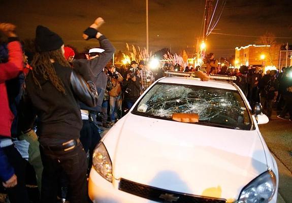 Varias personas golpean con ladrillos un coche en Ferguson. 
