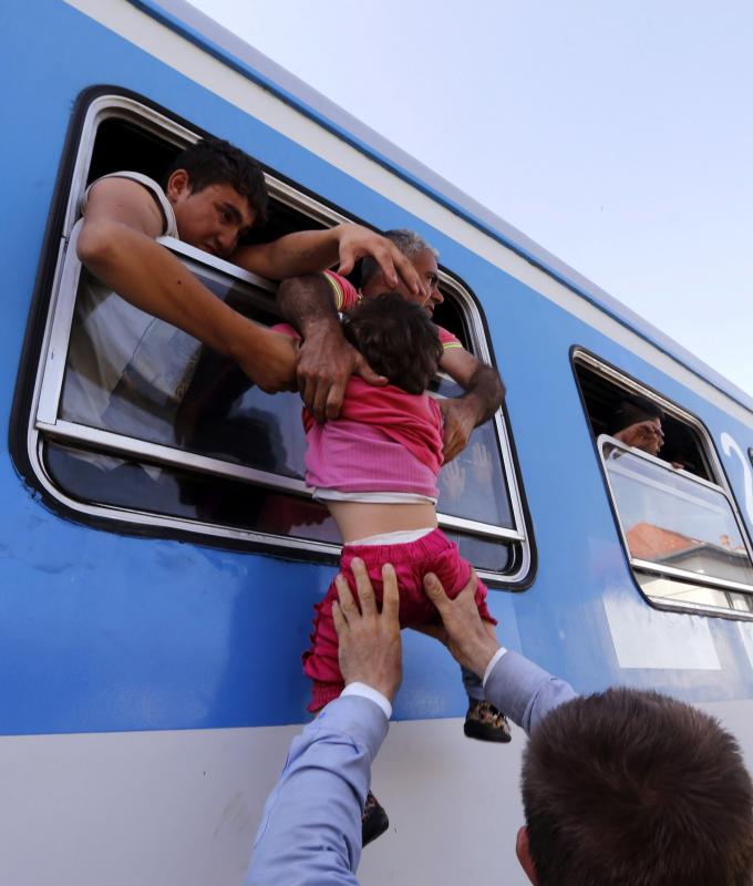 Un refugiado alza a su hija para que pueda entrar por la ventanilla y subir a bordo de un tren rumbo a Zagreb.