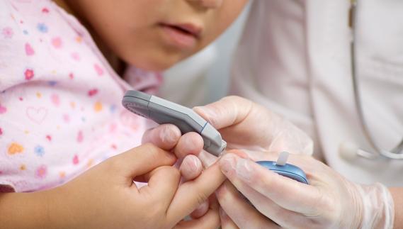 Un médico mide con un aparato la cantidad de azúcar en la sangre de un niño. 