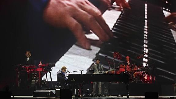 Elton John, sentado al piano y acompañado se sus músicos. 