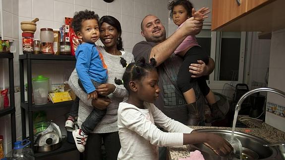 Marie y Jorge, con Óliver (un año y 9 meses) y Esmeralda (3) en brazos, mientras Emmanuella (6) friega una taza en su piso en Málaga