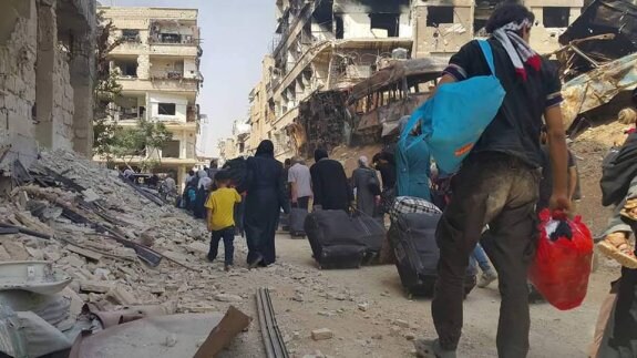 Una larga fila de vecinos de Daraya carga con algunos de sus enseres mientras abandonan la ciudad, liberada ayer de cuatro años de asedio. :: reuters