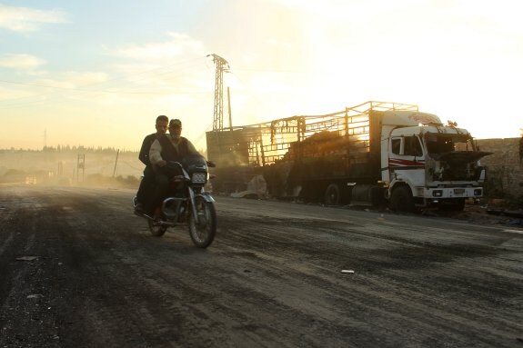 Dos hombres pasan con su moto frente al camión que transportaba ayuda humanitaria y que fue bombardeado en Alepo.
