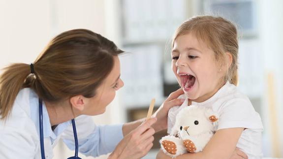 Una médico pediátra examina la garganta de una pequeña.