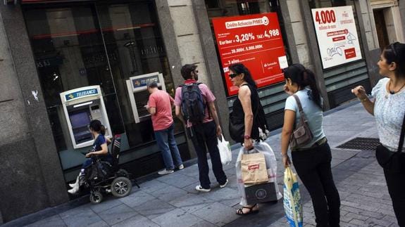 Varias personas hacen cola para sacar dinero de un cajero automático en una sucursal bancaria.