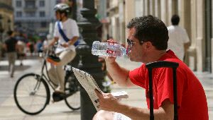 REFRESCARSE. Un hombre bebe agua sentado en un banco de la calle Larios, en la mañana de ayer. / CARLOS MORET