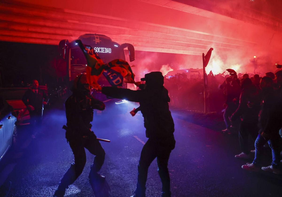 Un ertzaina se acerca a uno de los aficionados que se saltó el cordón policial en el recorrido del autobús de la Real Sociedad.