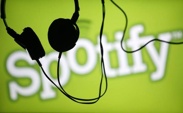 Unos auriculares delante del logotipo de Spotify. 