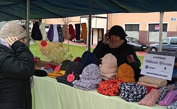 Maritxu Aranburu atiende a una cliente en su puesto de artesanía de la feria de Santa Lucía con el cartel donde se acepta abonar con monedas virtuales.