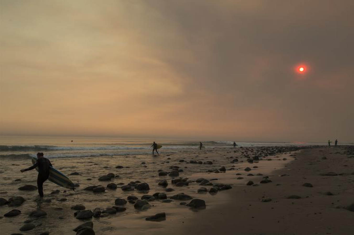 Un cielo lleno de humo alrededor de los surfistas. El fuego continúa creciendo y amenaza a las comunidades desde Carpinteria hasta Santa Barbara, California. El incendio se ha extendido a lo largo de 365 millas hasta el momento y ha destruido unas 800 estructuras desde que comenzó el 5 de diciembre en Ojai, California.