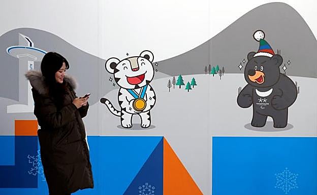 Una mujer revisa su teléfono mientras pasa junto a un anuncio de los Juegos de Pyeongchang. 