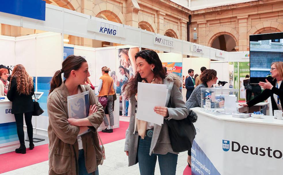 Dos jóvenes estudiantes recoplian información de los puestos informativos de las empresas en el Foro de Empleo de Deusto.