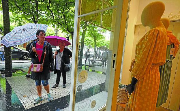 Dos mujeres observan, protegidas de la lluvia bajo el paraguas, el escaparate de la tienda Kett en el centro de San Sebastián. 