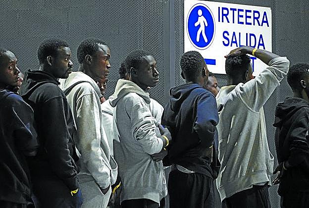 Los migrantes esperan pacientemente en cola a ser recogidos por las furgonetas de la Cruz Roja.