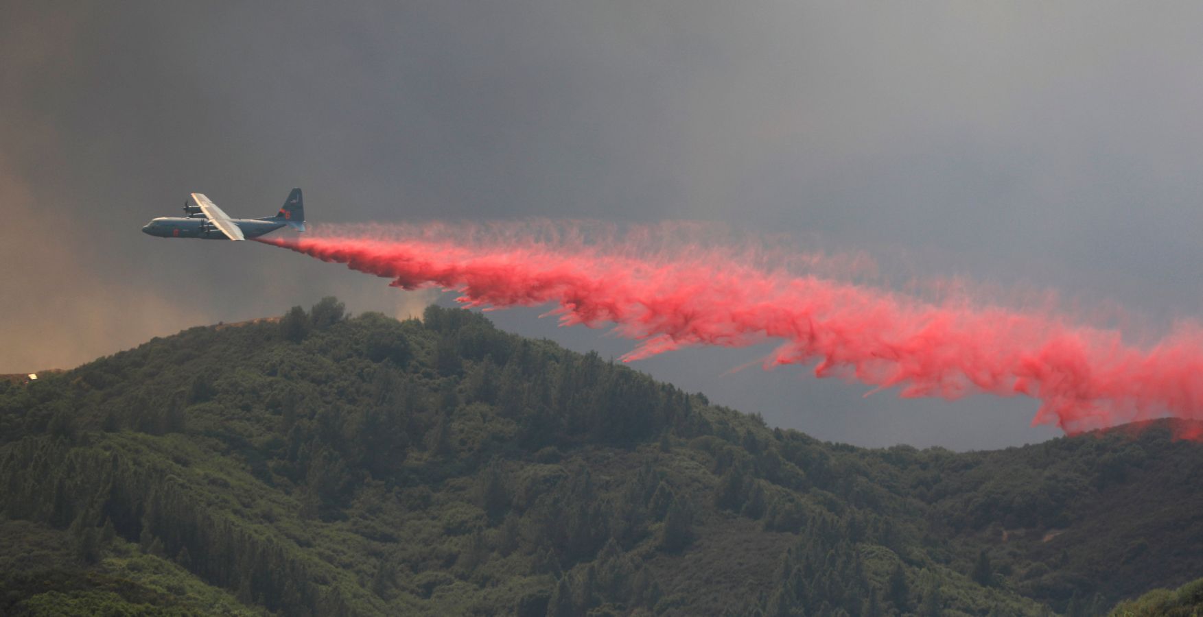 Un avión expulsa retardante rojo para frenar el fuego