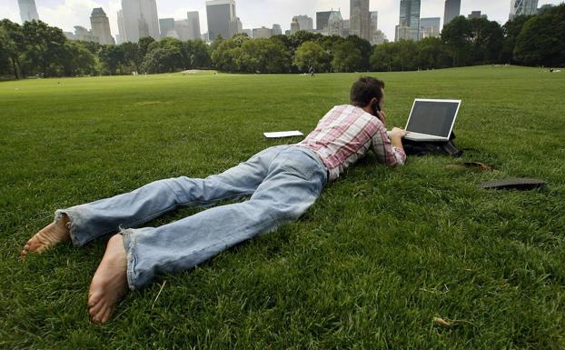 Un hombre trabaja con su ordenador portatil, mientras se toma un descanso en Central Park. 