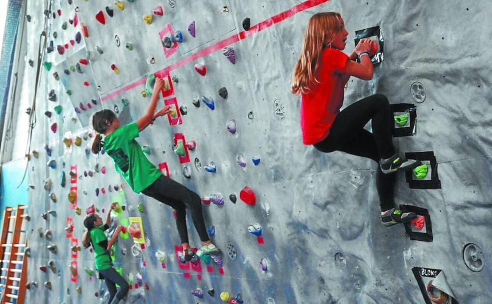 Tres chavalas en un rocódromo escalan superando los bloques de una pared.