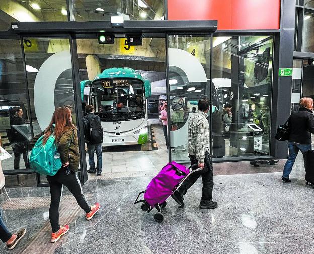 Pasajeros en la estación de autobuses caminan hacia sus autocares.