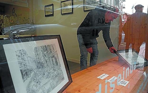 Exposición. Egurrola con sus dibujos, entre los reflejos del escaparate de Kokojaten. 