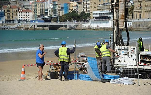 Un usuario de la playa pregunta a los operarios que están realizando catas bajo La Concha para las obras del Topo. 